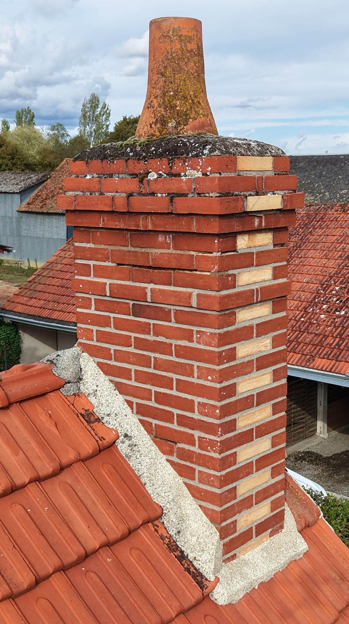 Vue aérienne rapprochée d’une cheminée en briques et de sa couverture, mettant en évidence l’état général des matériaux et les traces de vieillissement.